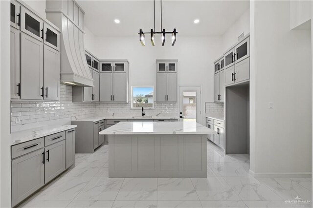 kitchen with premium range hood, a center island, sink, hanging light fixtures, and gray cabinetry