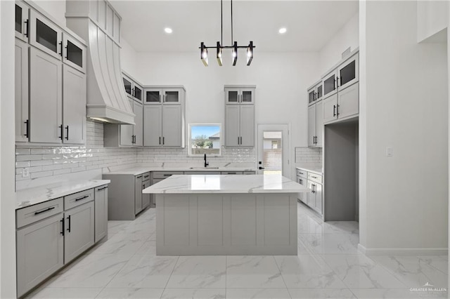 kitchen featuring gray cabinets, a kitchen island, pendant lighting, sink, and custom range hood