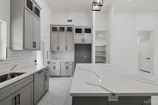 kitchen featuring tasteful backsplash, gray cabinets, pendant lighting, a center island, and light stone countertops