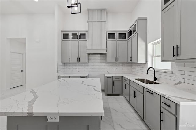 kitchen with marble finish floor, gray cabinetry, a kitchen island, a sink, and light stone countertops