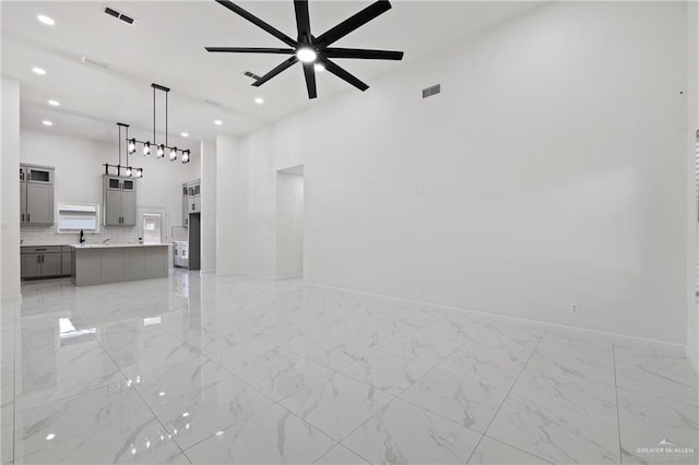 unfurnished living room with baseboards, marble finish floor, visible vents, and a ceiling fan