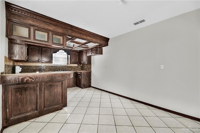 kitchen with sink, tasteful backsplash, kitchen peninsula, dark brown cabinets, and light tile patterned flooring