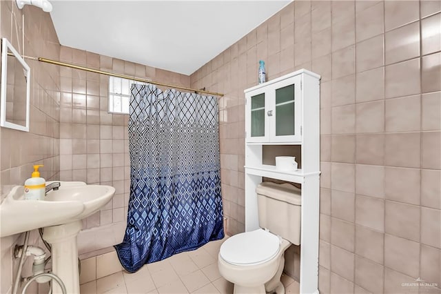 bathroom with toilet, a shower with curtain, tile patterned floors, and tile walls