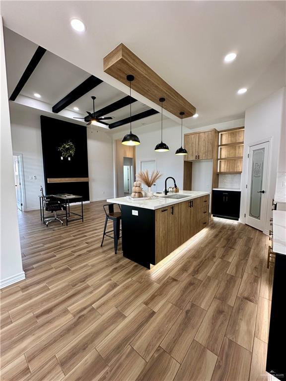 kitchen with decorative light fixtures, an island with sink, sink, ceiling fan, and beam ceiling