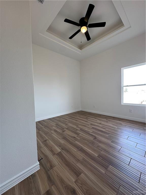 unfurnished room featuring ceiling fan, dark wood-type flooring, and a tray ceiling