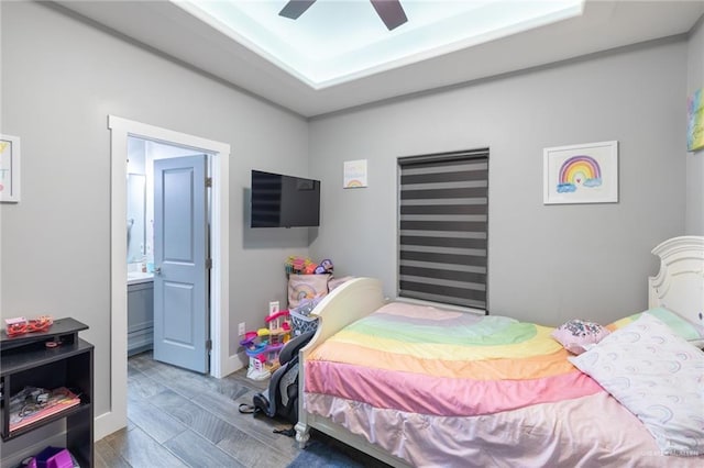 bedroom with a ceiling fan, a tray ceiling, and ensuite bath