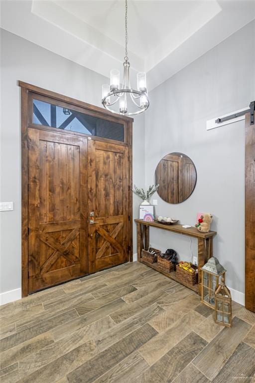 foyer featuring a tray ceiling, wood finish floors, a notable chandelier, a barn door, and baseboards