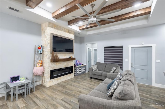 living area featuring beam ceiling, visible vents, a stone fireplace, and wood finished floors