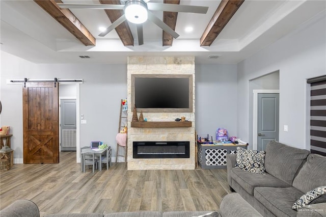 living room featuring a barn door, a fireplace, wood finished floors, and beam ceiling