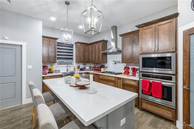 kitchen with wall chimney exhaust hood, appliances with stainless steel finishes, a breakfast bar area, a center island, and light countertops