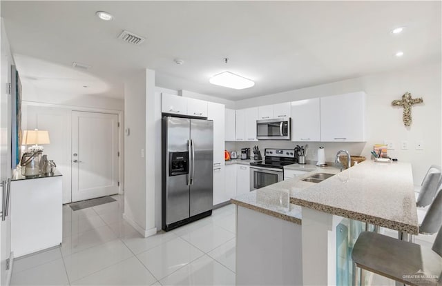 kitchen with stainless steel appliances, white cabinetry, a breakfast bar, and kitchen peninsula