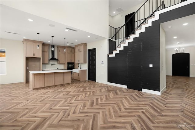 kitchen with light parquet floors, light brown cabinets, a towering ceiling, wall chimney range hood, and a kitchen island