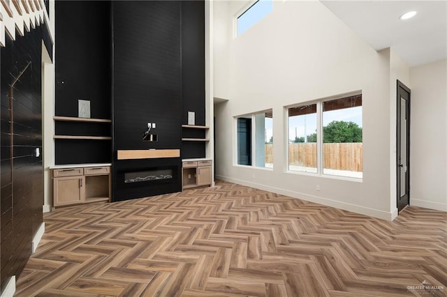 unfurnished living room featuring light parquet floors, a large fireplace, and a towering ceiling