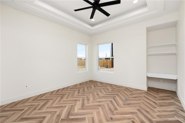 unfurnished bedroom with ceiling fan, light parquet floors, and a raised ceiling