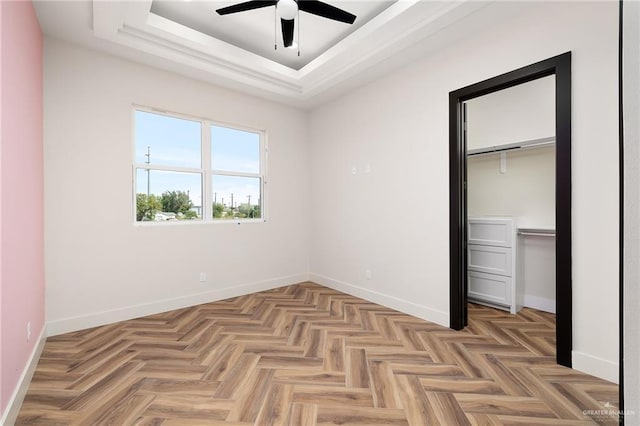 unfurnished bedroom with ceiling fan, a closet, a tray ceiling, and light parquet floors