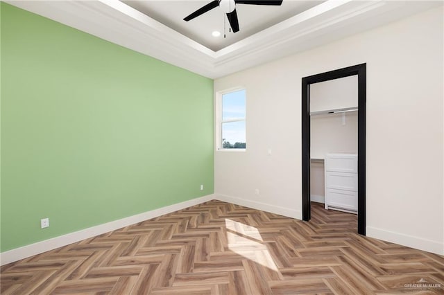 unfurnished bedroom featuring parquet flooring, ceiling fan, a tray ceiling, a closet, and a walk in closet