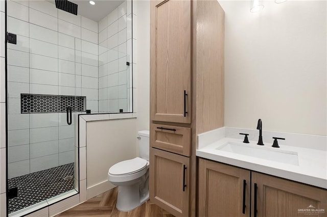 bathroom with toilet, a tile shower, vanity, and parquet flooring