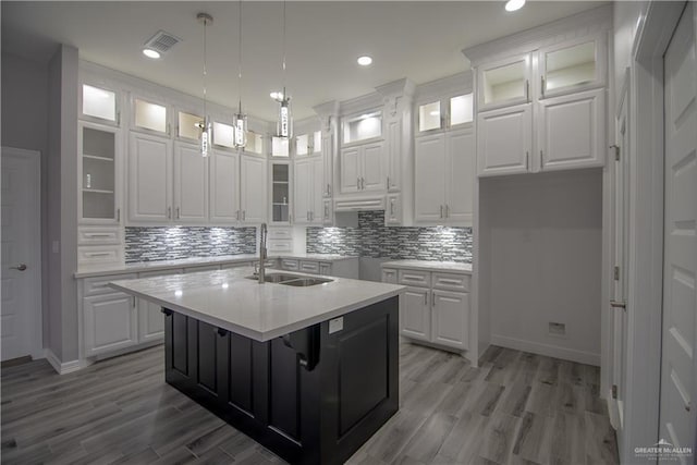 kitchen featuring visible vents, a center island with sink, white cabinetry, and a sink