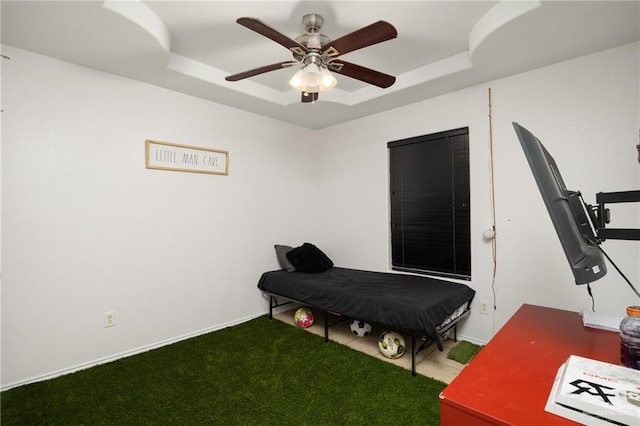 bedroom with a raised ceiling, ceiling fan, and carpet flooring