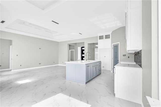 kitchen with a center island with sink, a tray ceiling, gray cabinets, sink, and white cabinetry