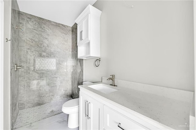 bathroom featuring vanity, a tile shower, and toilet