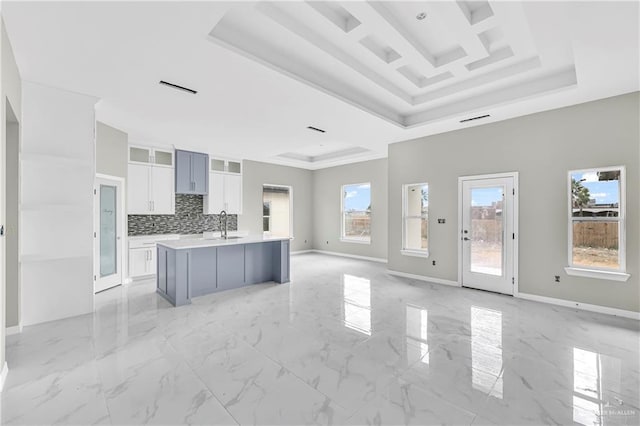 kitchen with tasteful backsplash, a kitchen island with sink, white cabinets, and a tray ceiling