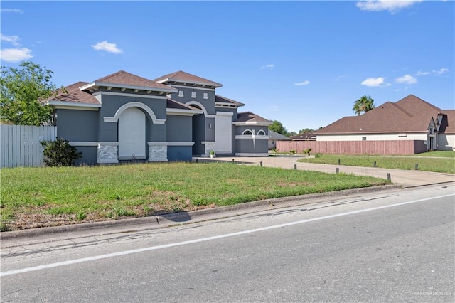mediterranean / spanish house with stucco siding, stone siding, fence, and a front lawn