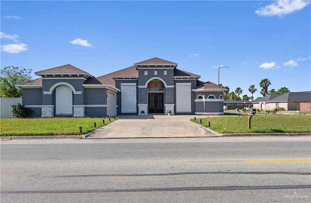mediterranean / spanish house featuring stucco siding, stone siding, a front lawn, french doors, and driveway