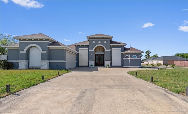 mediterranean / spanish house featuring a front yard, an attached garage, stone siding, concrete driveway, and french doors