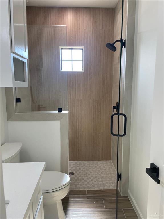 bathroom featuring hardwood / wood-style floors, vanity, toilet, and a shower with door