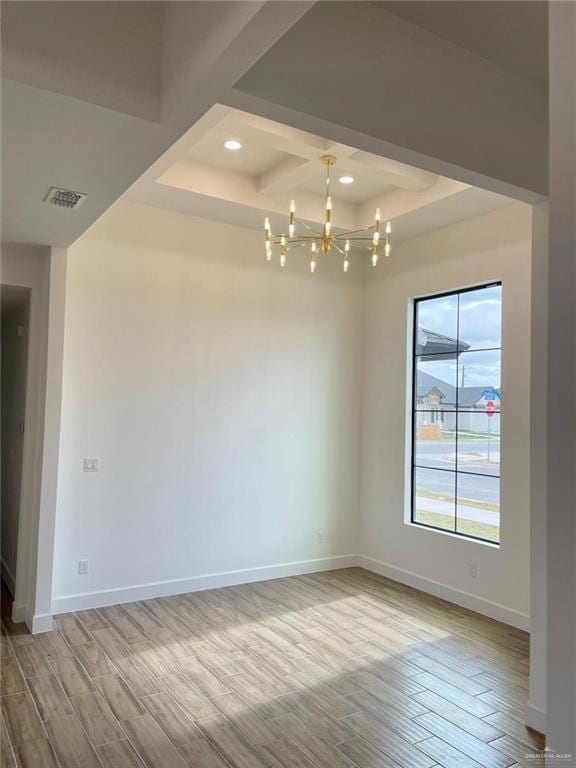 spare room with hardwood / wood-style flooring, a raised ceiling, and an inviting chandelier