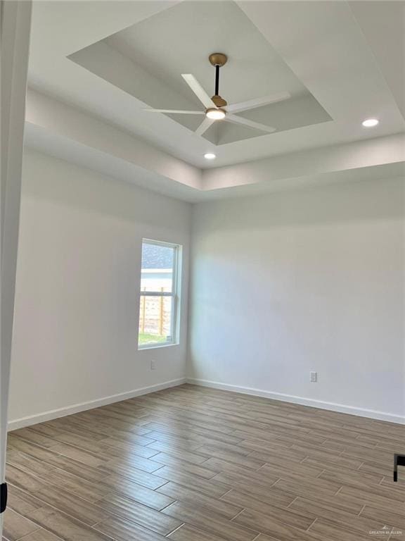 unfurnished room featuring a raised ceiling, ceiling fan, and light wood-type flooring