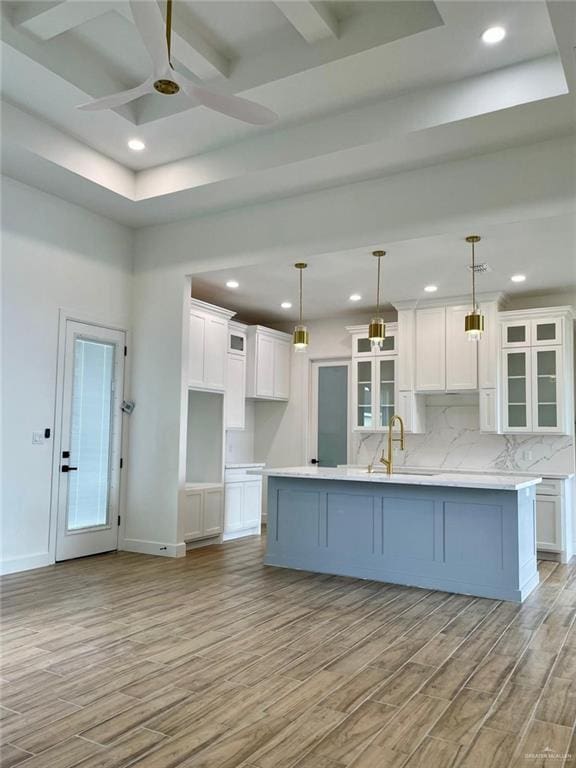 kitchen with a center island with sink, light hardwood / wood-style floors, white cabinetry, and hanging light fixtures