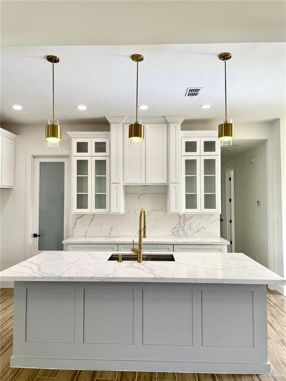 kitchen with a kitchen island with sink, light stone counters, sink, and pendant lighting