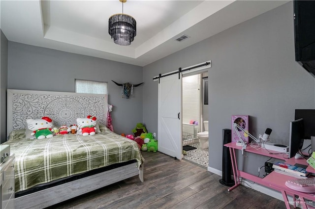 bedroom with dark hardwood / wood-style floors, a barn door, connected bathroom, and a tray ceiling