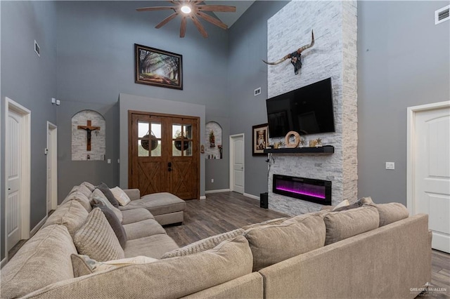 living room featuring hardwood / wood-style floors, ceiling fan, a stone fireplace, and high vaulted ceiling