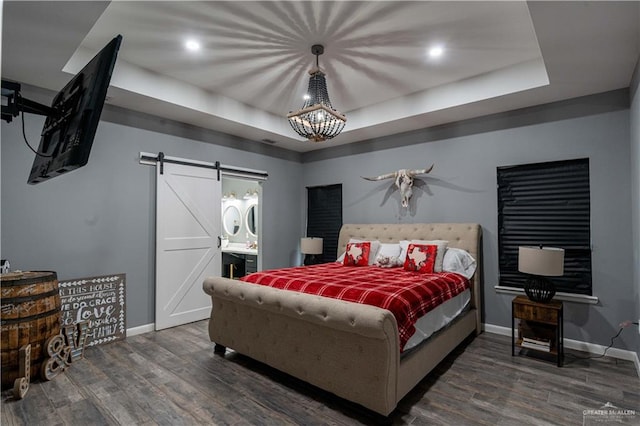 bedroom featuring a tray ceiling, a barn door, dark hardwood / wood-style flooring, and ensuite bath