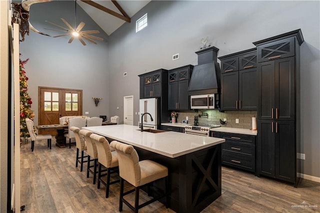 kitchen featuring a kitchen breakfast bar, stainless steel appliances, wood-type flooring, high vaulted ceiling, and an island with sink