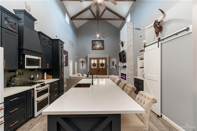 kitchen with stainless steel appliances, sink, a barn door, high vaulted ceiling, and a breakfast bar area