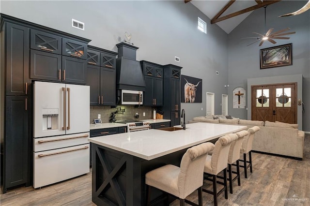 kitchen featuring high vaulted ceiling, light wood-type flooring, an island with sink, and appliances with stainless steel finishes