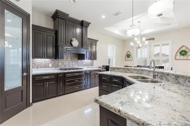 kitchen featuring tasteful backsplash, a tray ceiling, sink, decorative light fixtures, and stainless steel gas stovetop