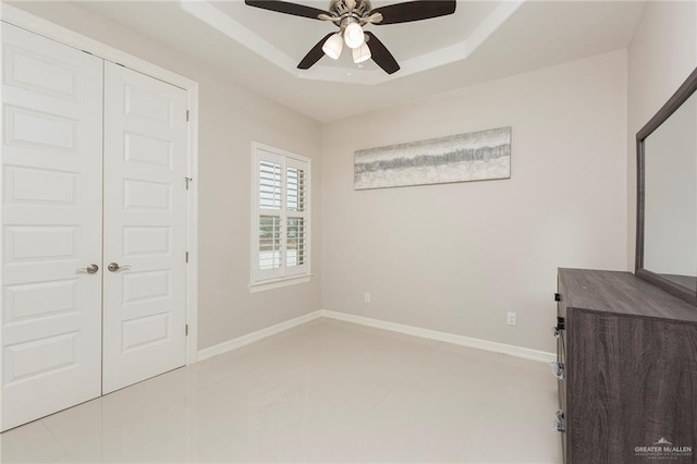 unfurnished bedroom with ceiling fan, a raised ceiling, and a closet