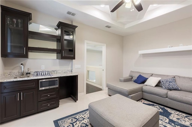 living room with ceiling fan, light tile patterned floors, sink, and a tray ceiling