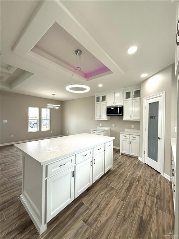 kitchen featuring light stone countertops, a raised ceiling, white cabinets, a kitchen island, and hanging light fixtures