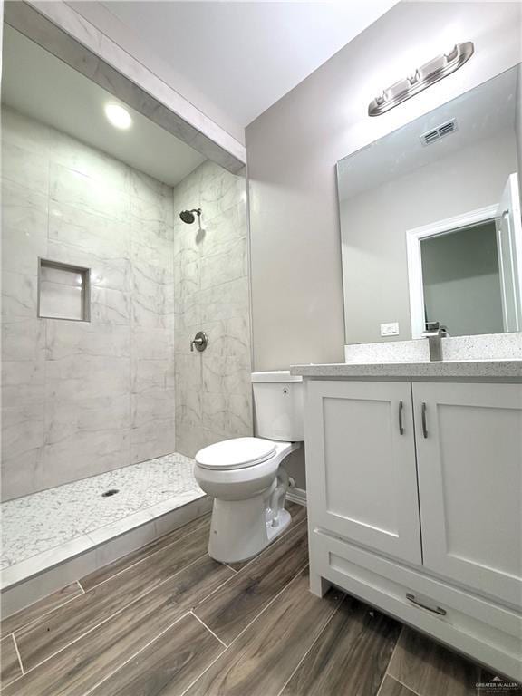 bathroom featuring a tile shower, vanity, and toilet