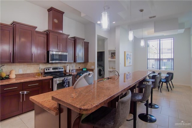 kitchen featuring a kitchen bar, appliances with stainless steel finishes, decorative light fixtures, and an island with sink