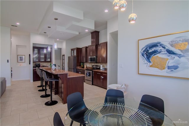 kitchen featuring decorative backsplash, light stone counters, stainless steel appliances, a center island with sink, and hanging light fixtures