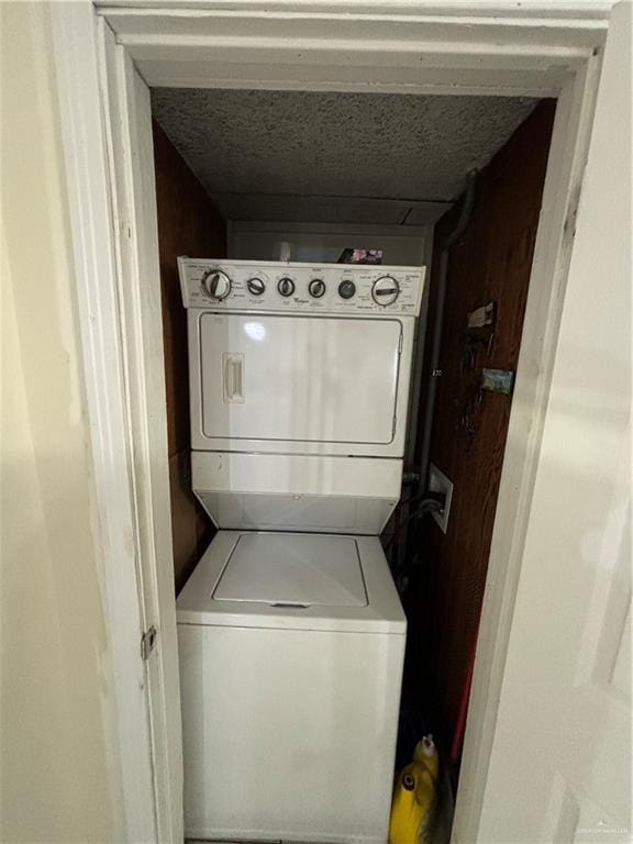 laundry room featuring a textured ceiling and stacked washer / drying machine