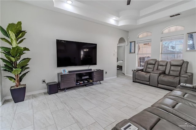 living room featuring arched walkways, a raised ceiling, visible vents, and baseboards