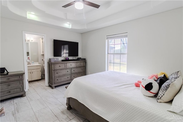 bedroom featuring ensuite bathroom, a sink, a ceiling fan, marble finish floor, and a raised ceiling